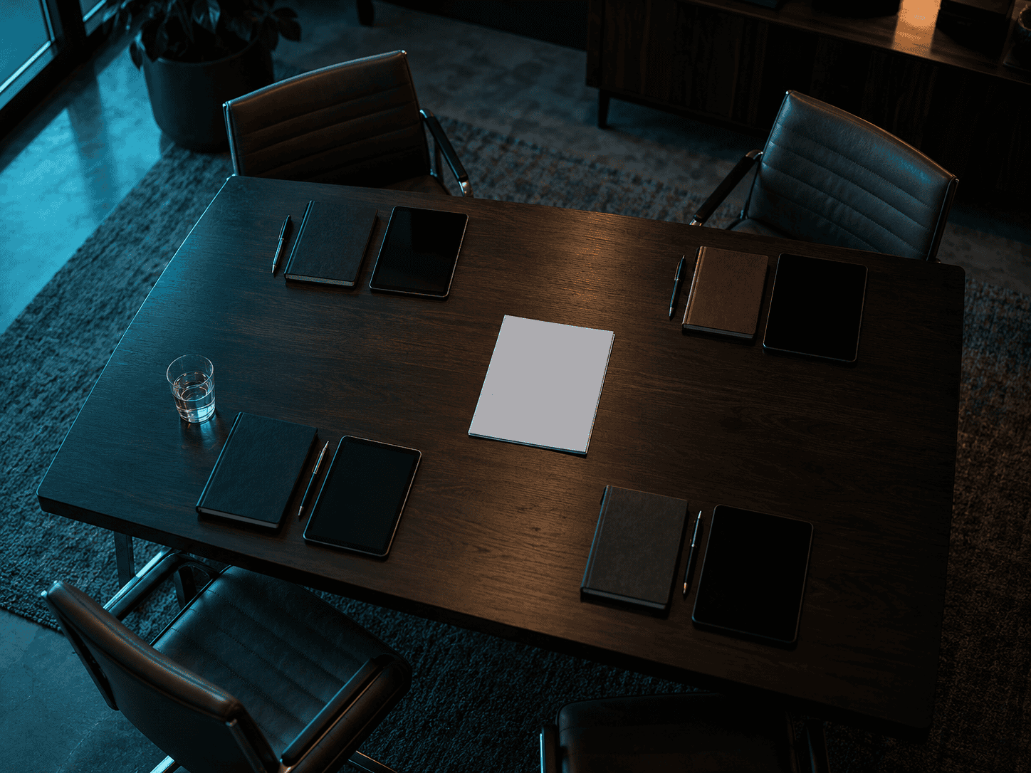 A meeting table seen from above with four notebooks and tablets arranged around it